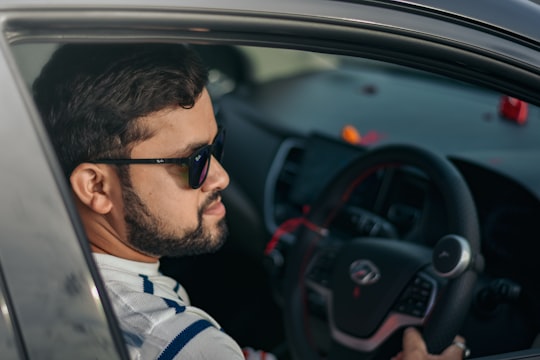 man in white and blue stripe polo shirt driving car in Chikhli India