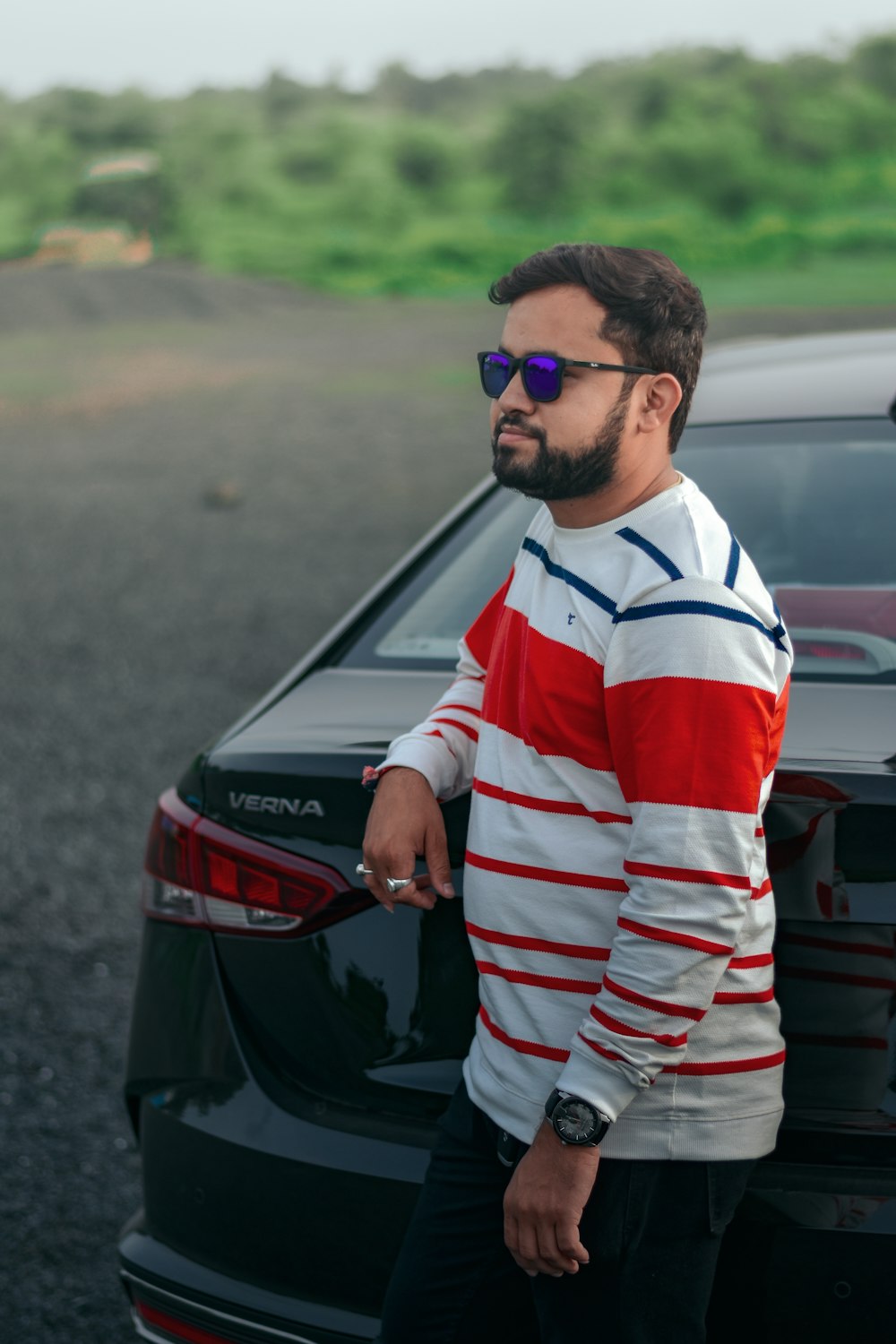 man in white red and black striped long sleeve shirt standing beside black car