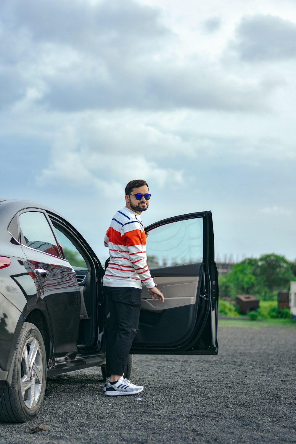 man in white and orange striped polo shirt and black pants leaning on black car