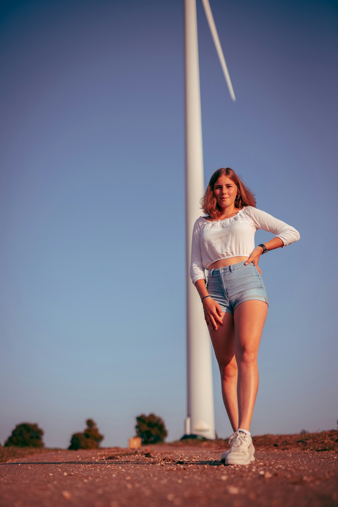 woman in white shirt and blue denim shorts standing on white metal pole during daytime