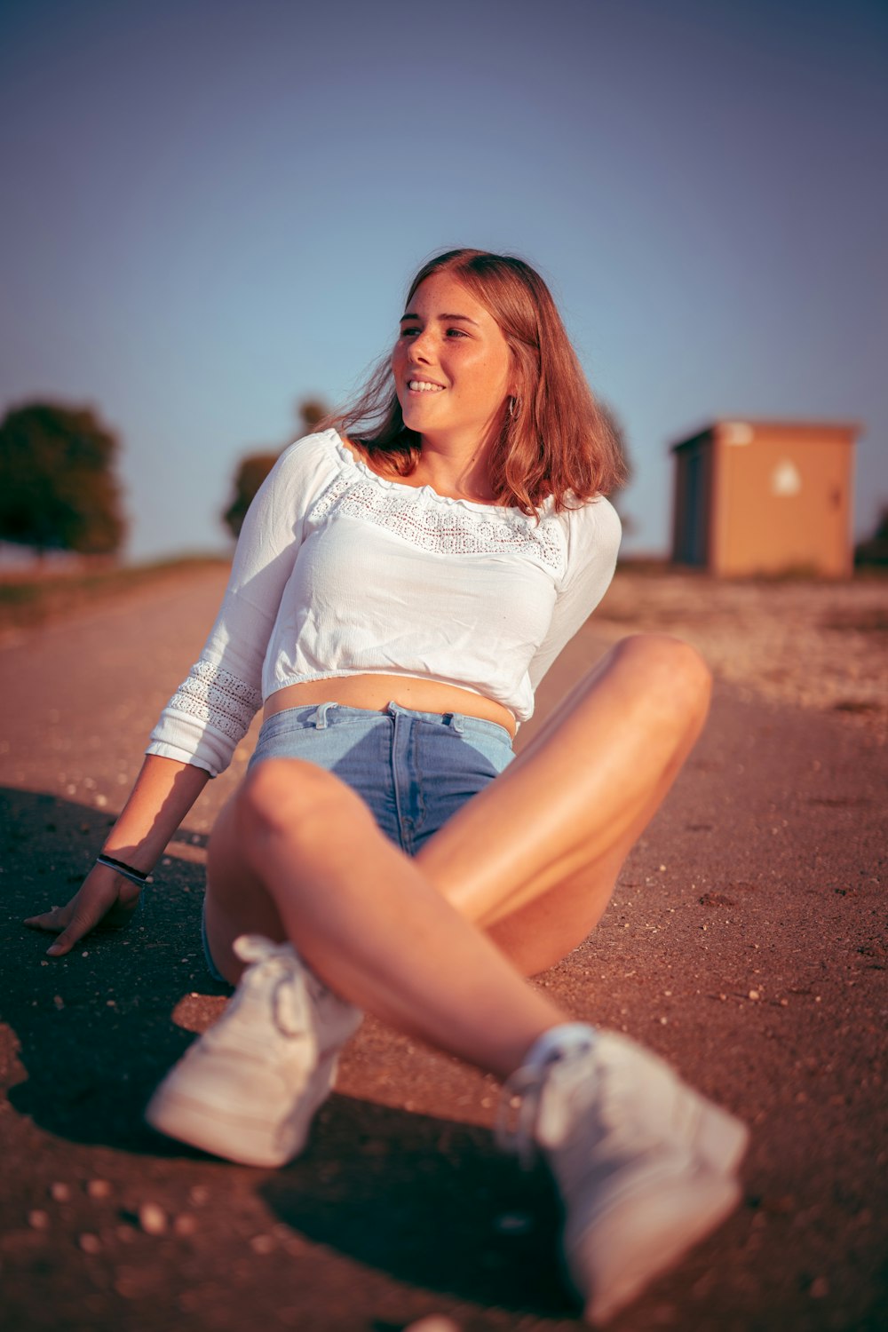 woman in white long sleeve shirt and blue denim shorts sitting on brown dirt road during