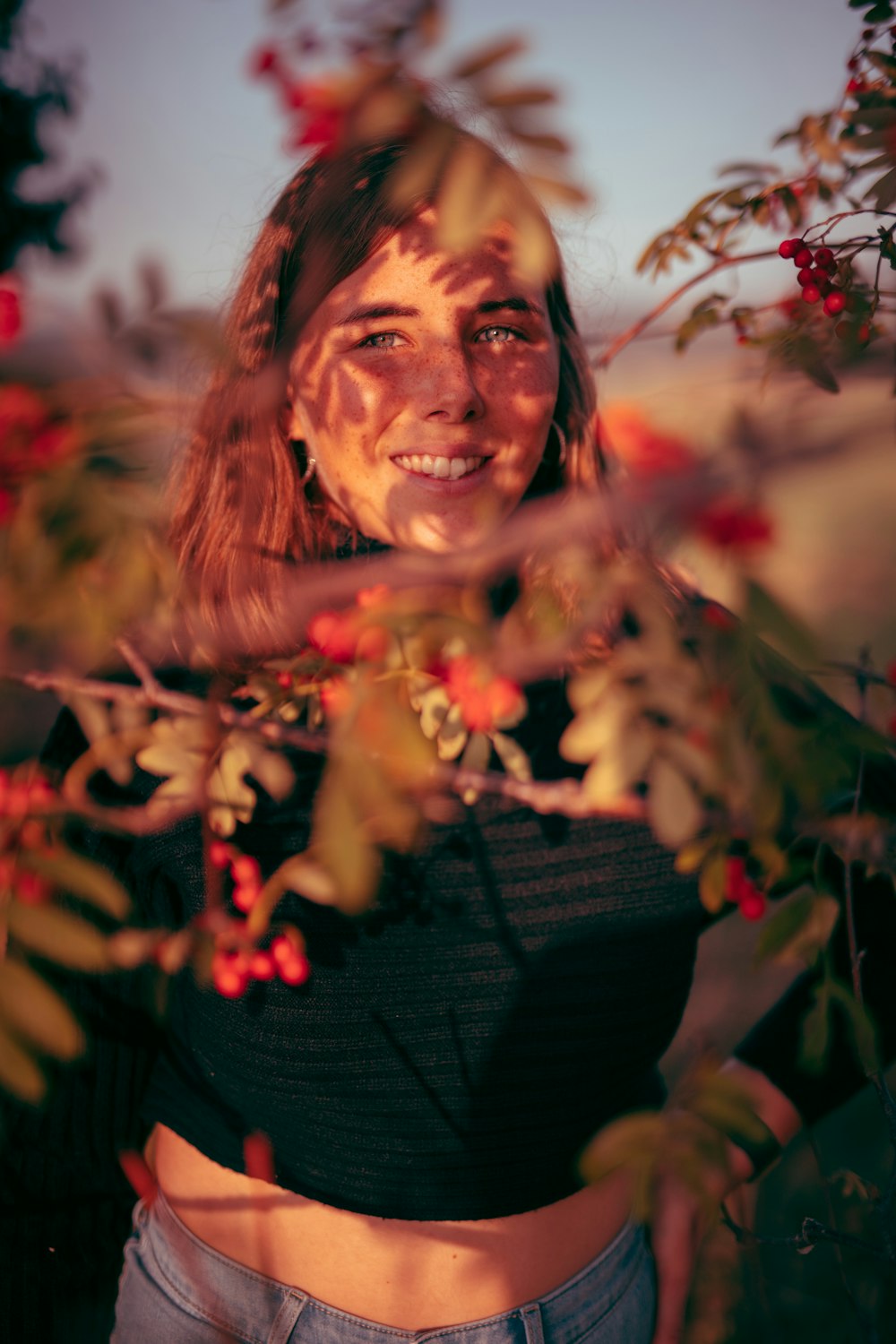 woman in black knit sweater standing beside red flowers