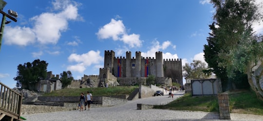 people walking on gray concrete pathway near gray concrete building under blue sky during daytime in Castelo de Óbidos Portugal