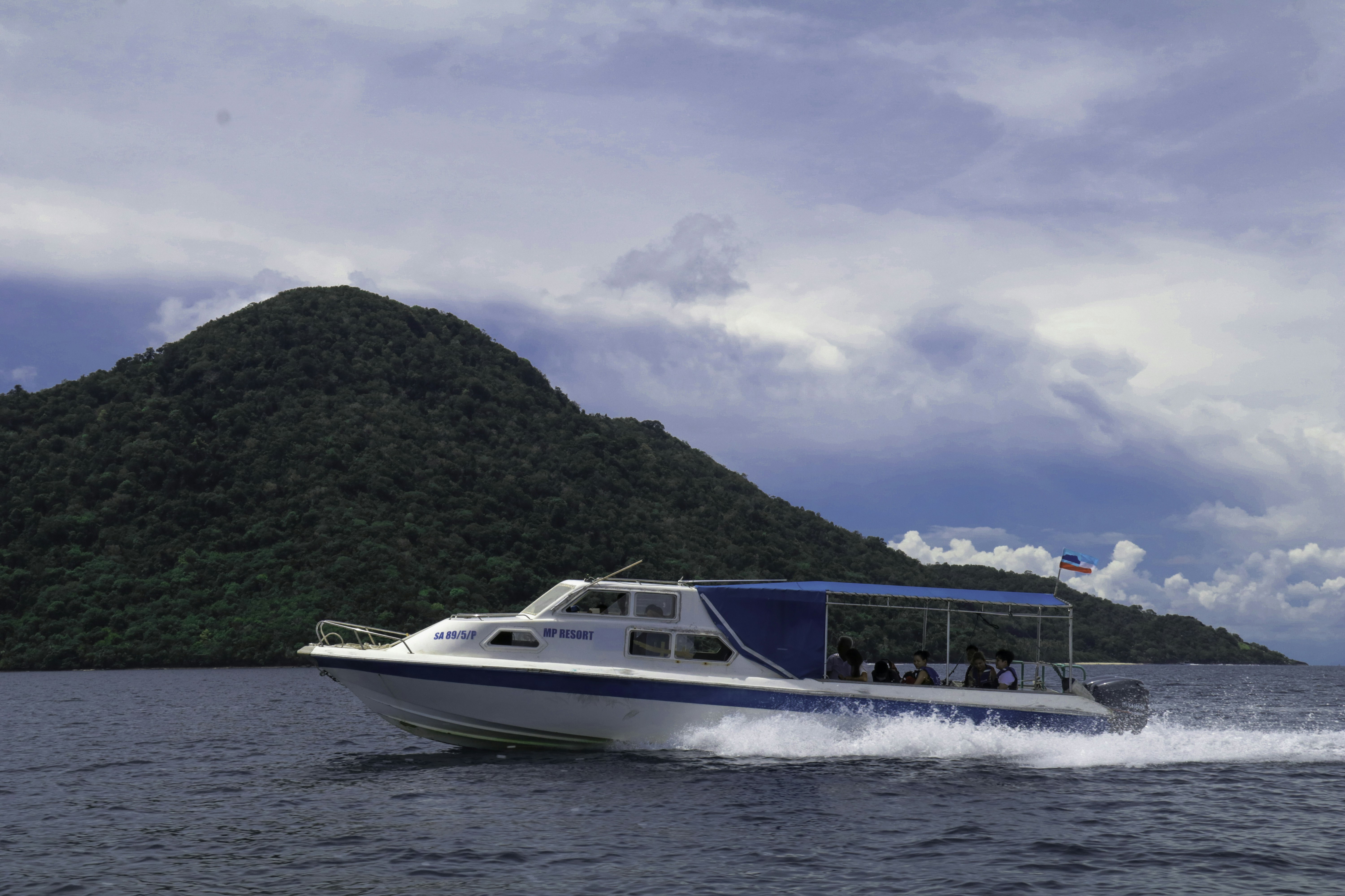 white and blue boat on sea near mountain under white clouds and blue sky during daytime