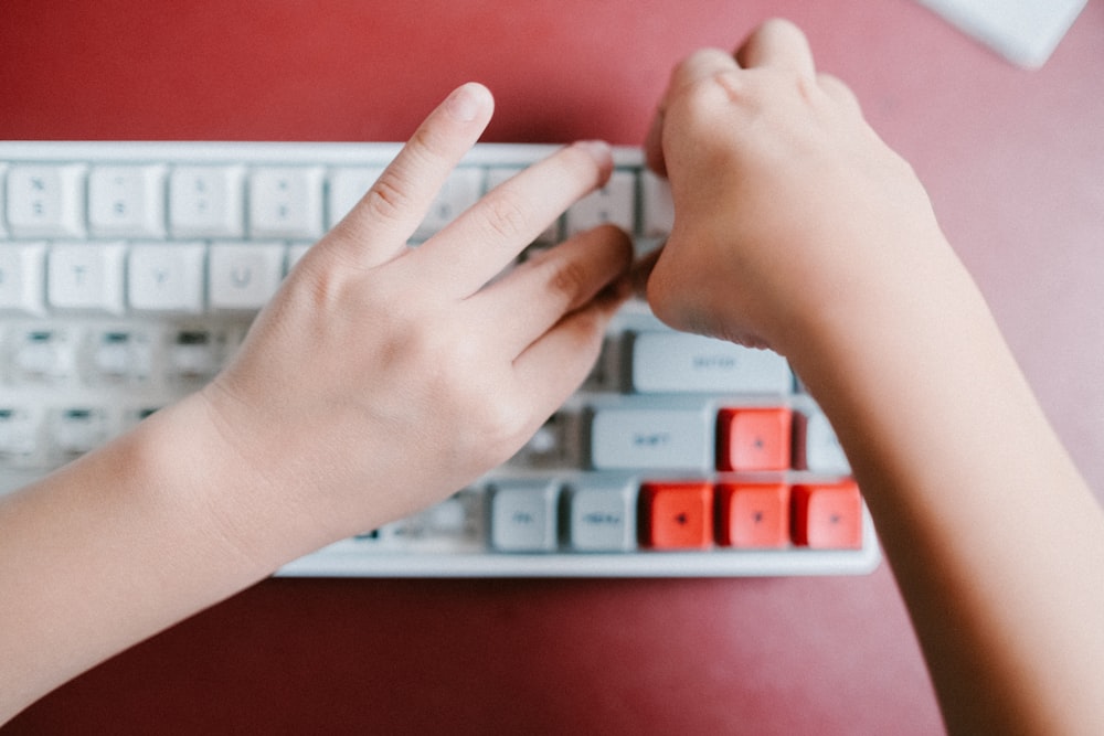 Mano izquierda de las personas en el teclado rojo y blanco de la computadora