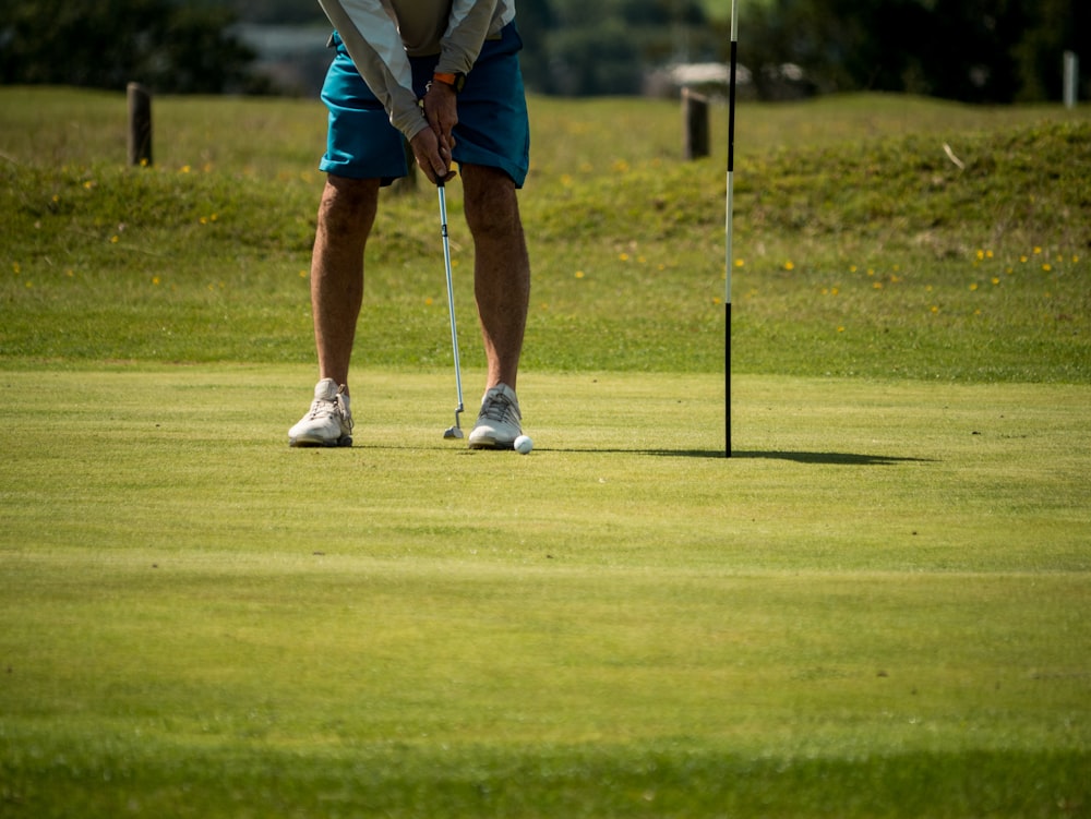 Hombre con camisa blanca y pantalones cortos azules jugando al golf durante el día