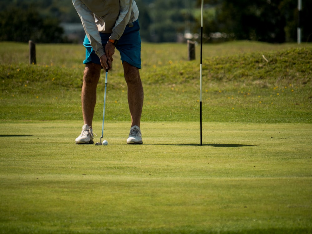 흰색 셔츠와 파란색 반바지를 입은 남자가 낮에 골프를 치고 있다