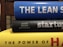 A stack of three books with colorful spines. The top book is blue with the title 'THE LEAN S'. The middle book has a black cover with the word 'startup' written on it and authors listed underneath. The bottom book is yellow, partially showing the title 'THE POWER OF H'. The books are stacked horizontally in a close-up view.