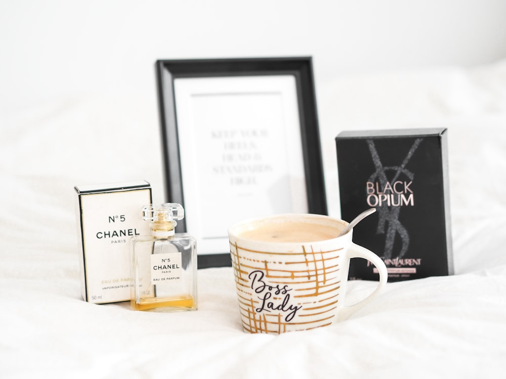 a white bed topped with a cup of coffee next to a box of perfume