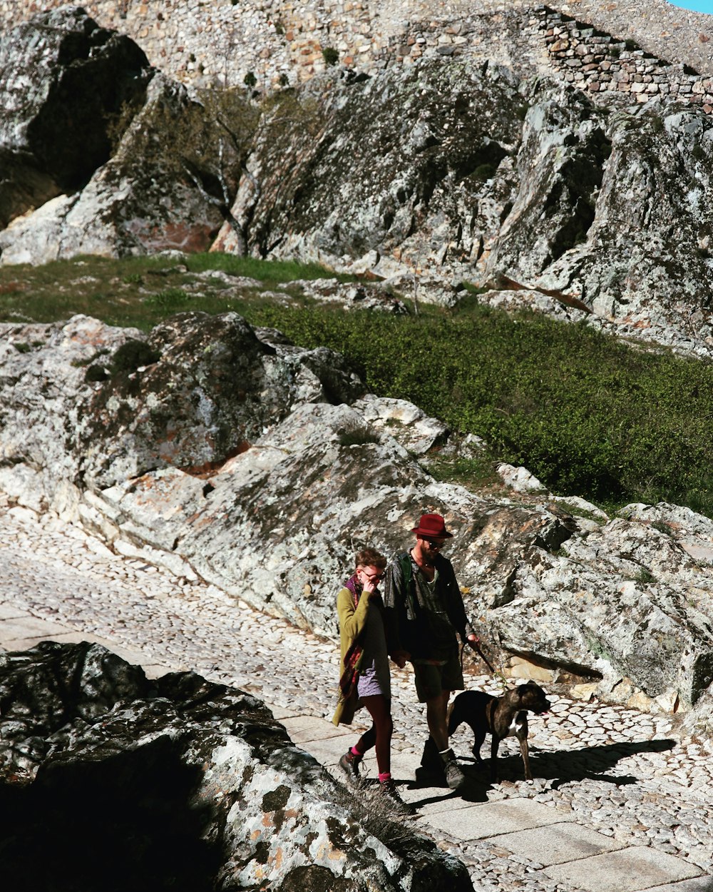 woman in red jacket standing beside black and brown short coated dog on rocky mountain during