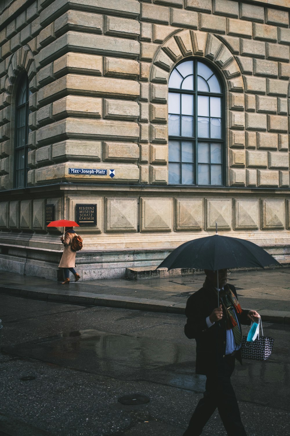 woman in black jacket holding umbrella walking on sidewalk during daytime