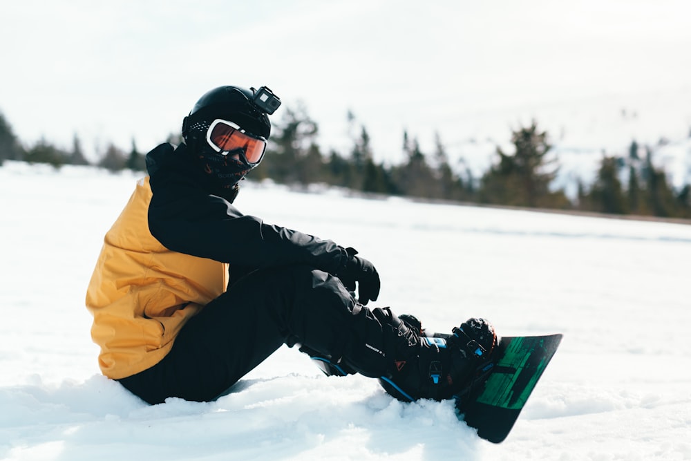 person in yellow jacket and black pants riding on snowboard