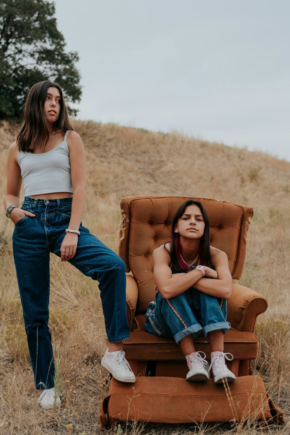 woman in white tank top and blue denim jeans sitting on brown armchair