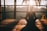 A person is sitting cross-legged, meditating on a wooden platform with a serene view of trees and a large sun setting in the background. The warm light creates a tranquil and peaceful atmosphere, casting soft shadows around the individual.