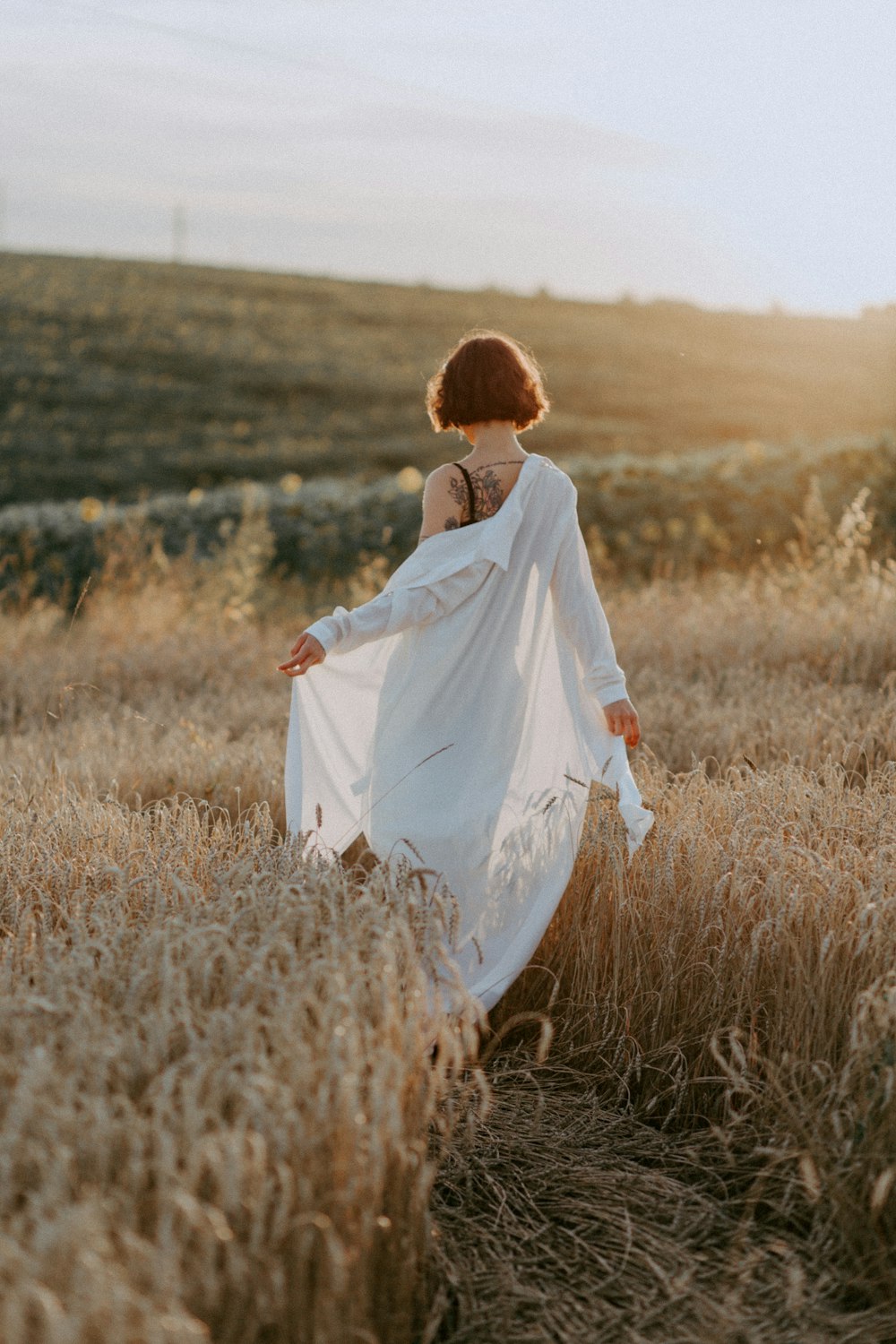 femme en robe blanche marchant sur le champ d’herbe brune pendant la journée