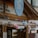 A quaint café shop with a wooden exterior is adorned with colorful string lights shaped like spheres, in pastel shades of pink, blue, and gray. A large circular sign with the words 'Café Shop' is prominently displayed above the entrance.