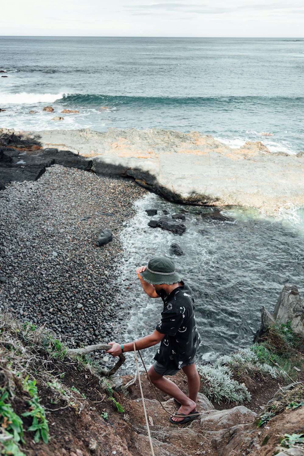 man in black jacket and orange cap standing on rocky shore during daytime