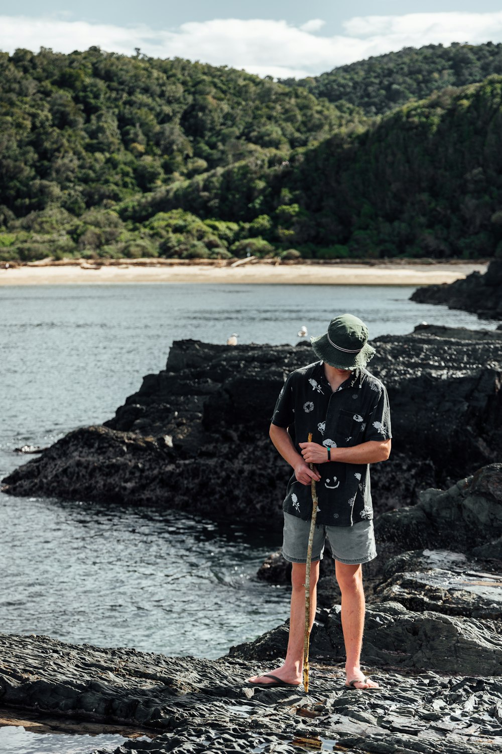 man in blue t-shirt and gray shorts standing on rocky shore during daytime