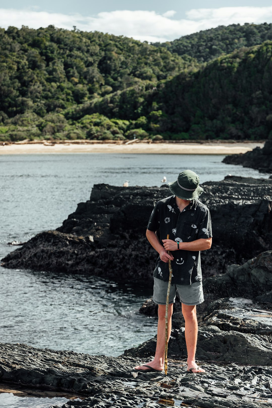 man in blue t-shirt and gray shorts standing on rocky shore during daytime