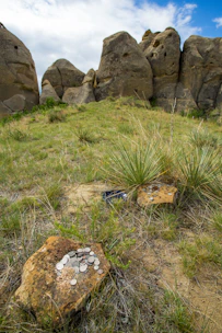 A treasure hunter scanning rocky terrain with a long-range metal detector under a clear blue sky.