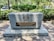 A memorial plaque set on a large stone block, surrounded by trees and greenery. The plaque contains a menorah symbol and text dedicating the site to James Edward Oglethorpe for the Savannah Jewish Community. Small stones are placed on top of the memorial.