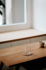 An assortment of wooden coasters and cups arranged on a natural wood table with soft sunlight.