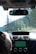 The interior of a car showing the driver's view with the steering wheel and dashboard visible. A person’s hand is on the steering wheel. The in-car navigation system is active and displaying a map on the screen. There are trees and greenery visible through the windshield, indicating an outdoor, possibly scenic, environment.