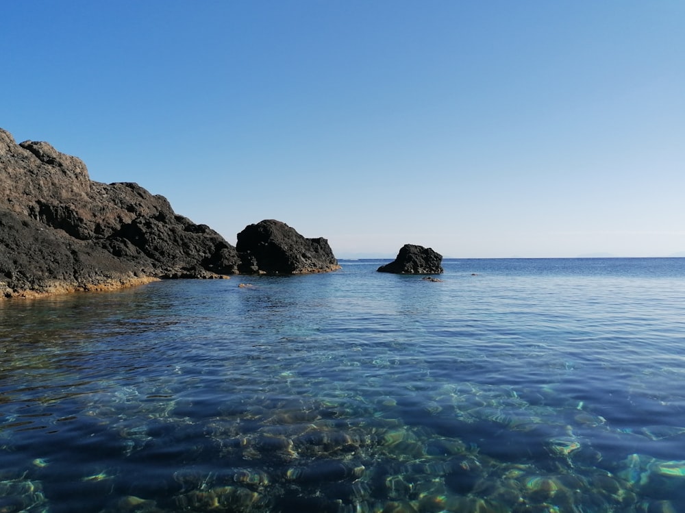 black rock formation on body of water during daytime