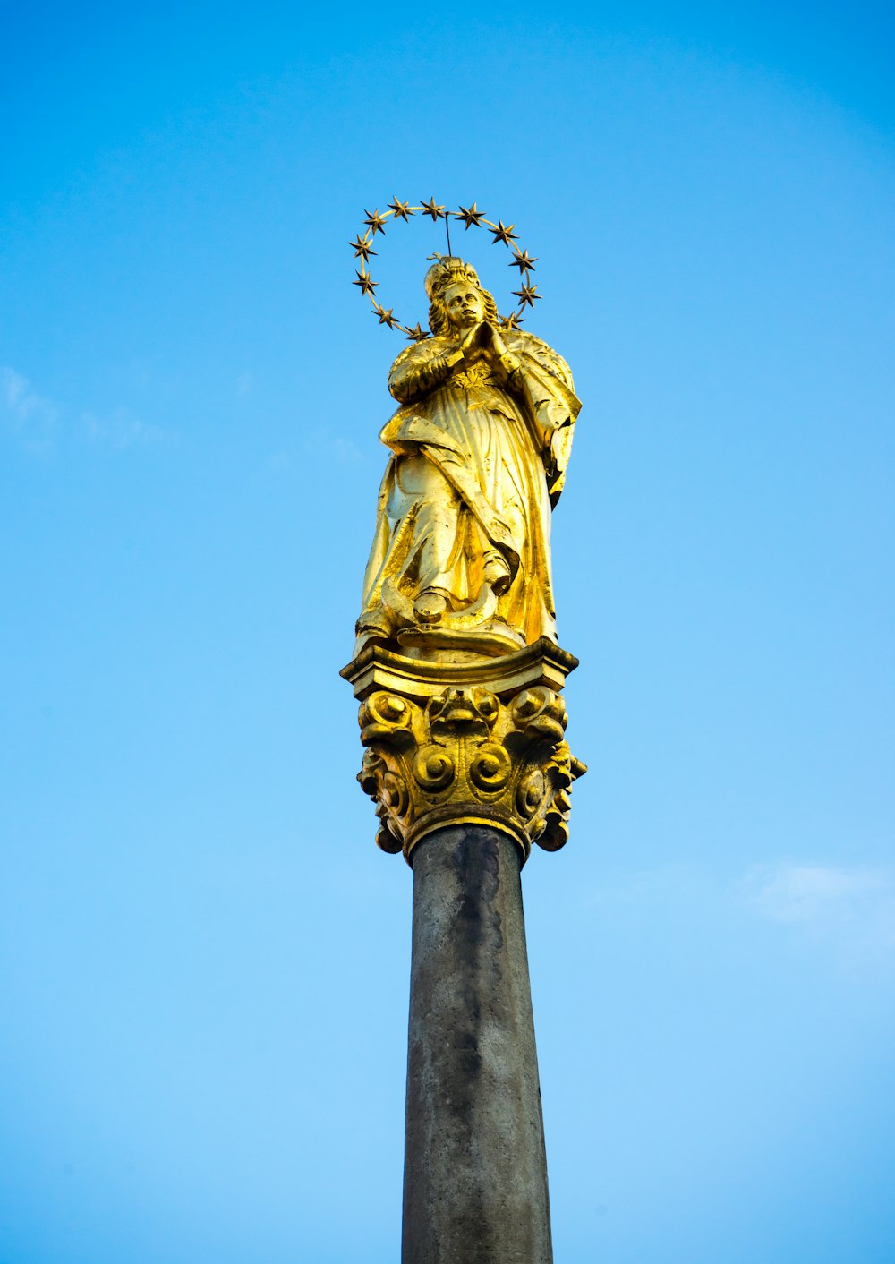 gold statue of man holding book under blue sky during daytime