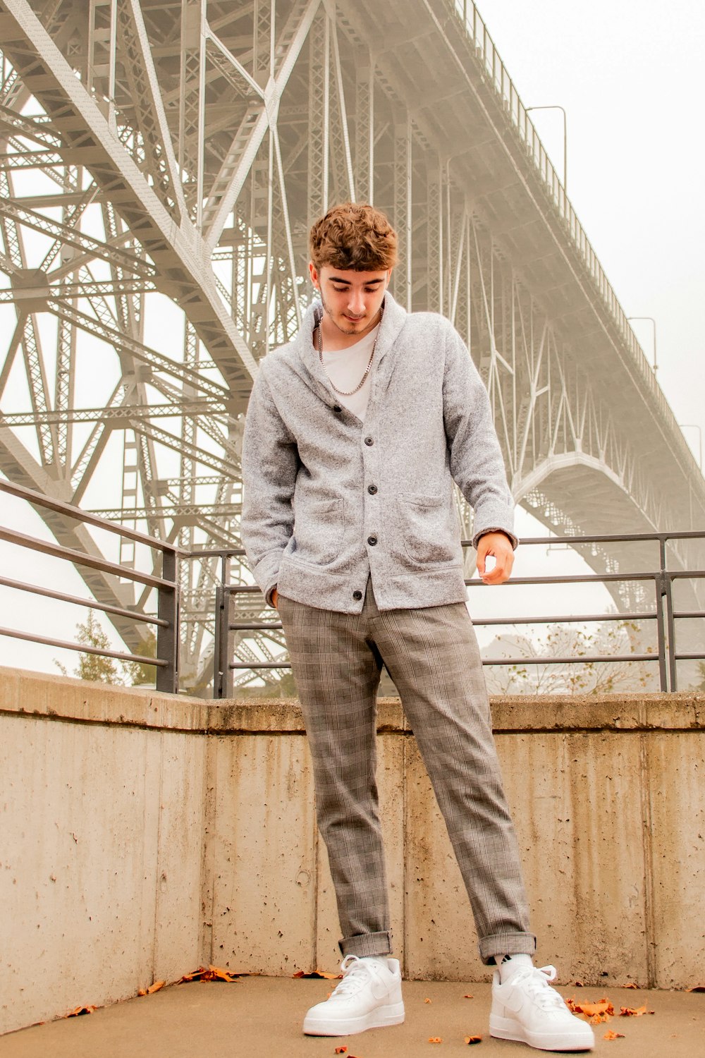 man in gray dress shirt and blue denim jeans standing on white metal bridge