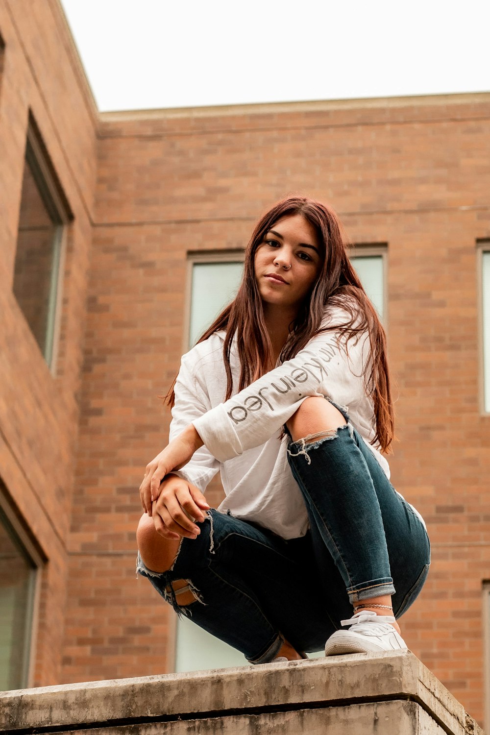 woman in white long sleeve shirt and blue denim jeans sitting on brown concrete wall during