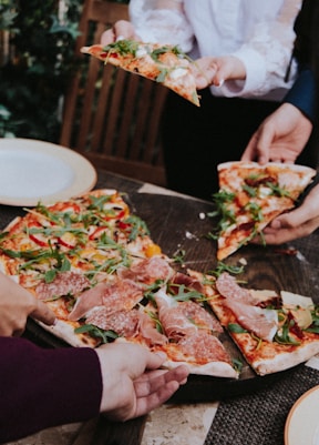 person holding pizza with cheese and green leaves