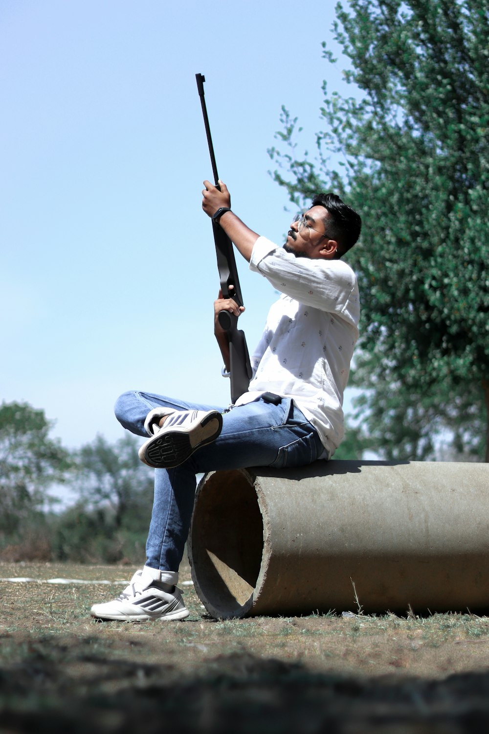 man in white dress shirt and blue denim jeans sitting on brown wooden post during daytime