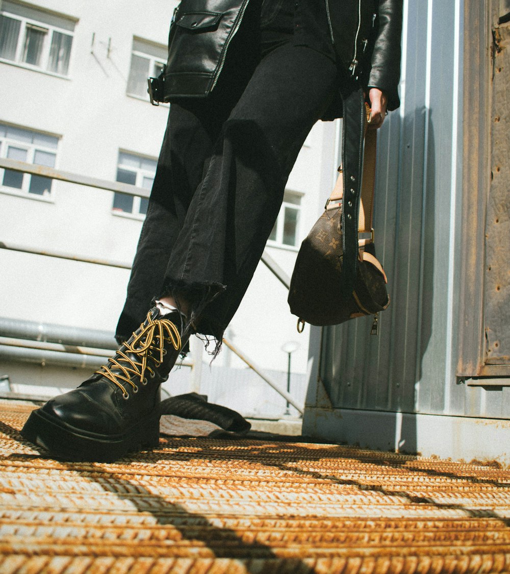person in black pants and black leather boots standing on brown and beige carpet