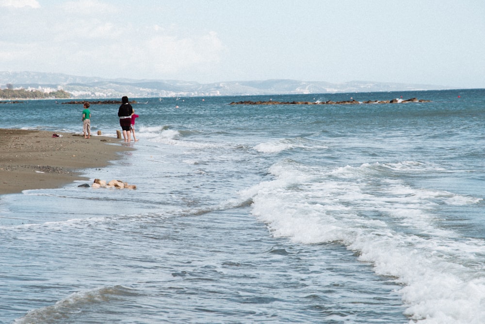 2 men and woman standing on beach during daytime