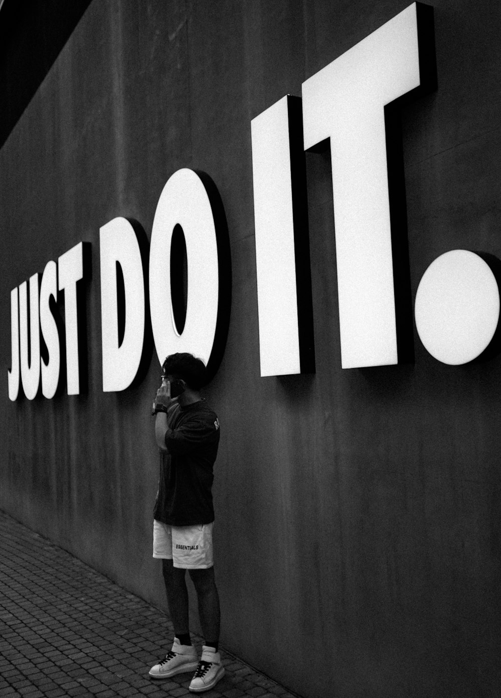 grayscale photo of man in black jacket standing near wall