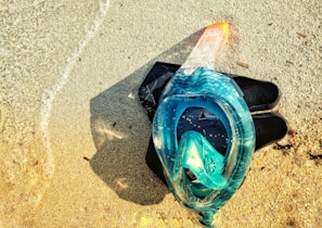 A set of swim fins and a snorkel laid out on a white towel beside turquoise water.