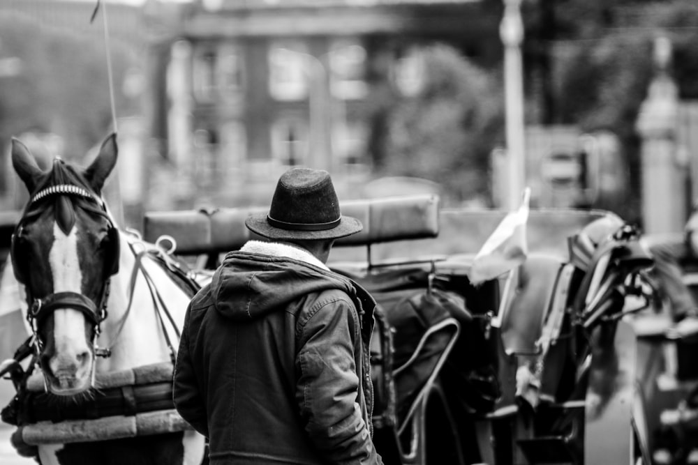 grayscale photo of man in jacket and hat sitting on motorcycle