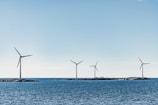 A serene coastal scene with four wind turbines positioned on small islands amidst a blue sea. The sky is clear and bright, contributing to the tranquil atmosphere.