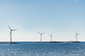 A serene coastal scene with four wind turbines positioned on small islands amidst a blue sea. The sky is clear and bright, contributing to the tranquil atmosphere.