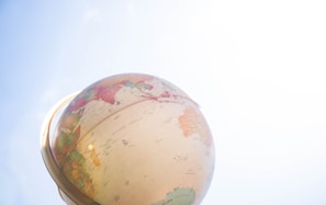 A globe depicting continents and oceans is positioned against a clear blue sky. The sunlight highlights parts of the globe, casting a bright and serene atmosphere.