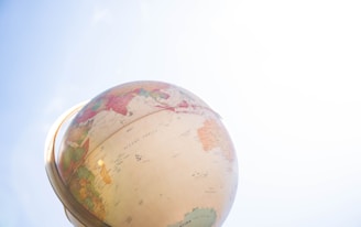 A globe depicting continents and oceans is positioned against a clear blue sky. The sunlight highlights parts of the globe, casting a bright and serene atmosphere.