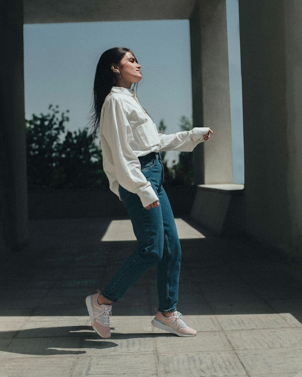 woman in white long sleeve shirt and blue denim jeans standing on gray concrete floor during