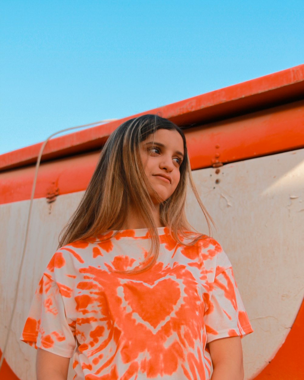 woman in orange and white floral shirt standing beside white wall during daytime