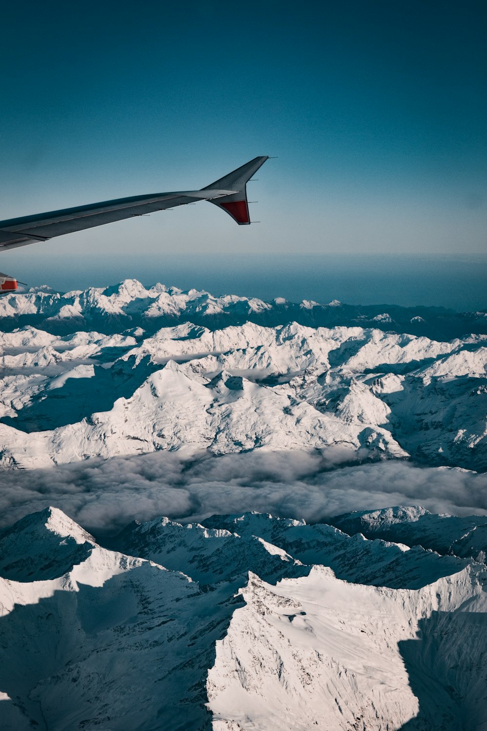 雪に覆われた山の上空を飛ぶ赤と白の飛行機の翼