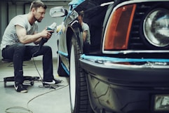 A friendly car detailer smiling while polishing a shiny black car under soft natural light.