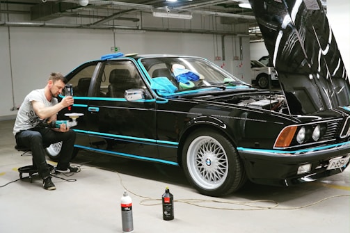 man in black jacket and black pants standing beside blue car