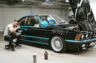 man in black jacket and black pants standing beside blue car