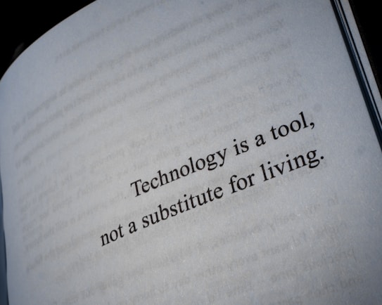 A close-up view of a book page with the text 'Technology is a tool, not a substitute for living.' printed in black letters.