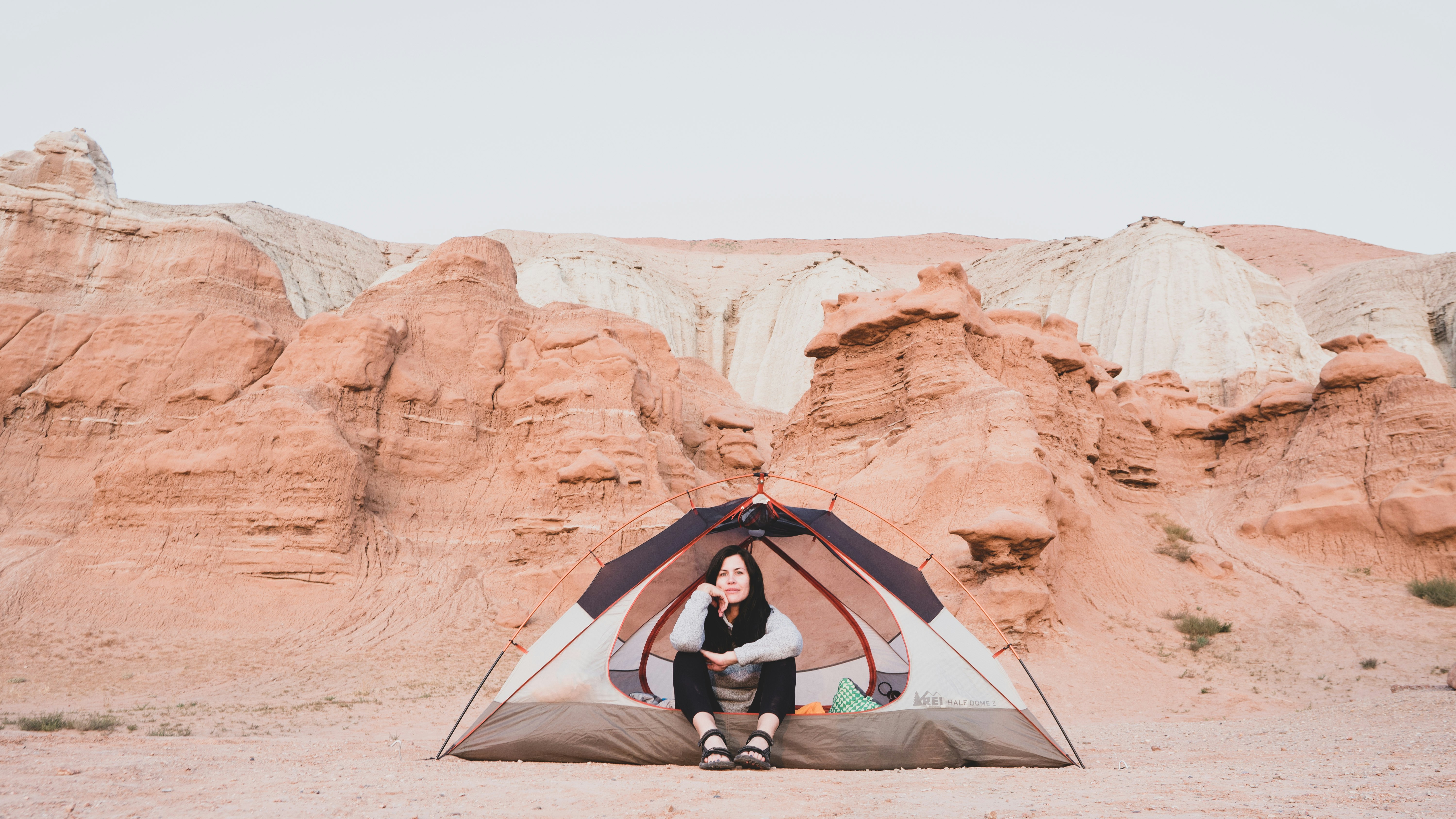 man in black jacket and gray pants sitting on gray dome tent on brown rock formation